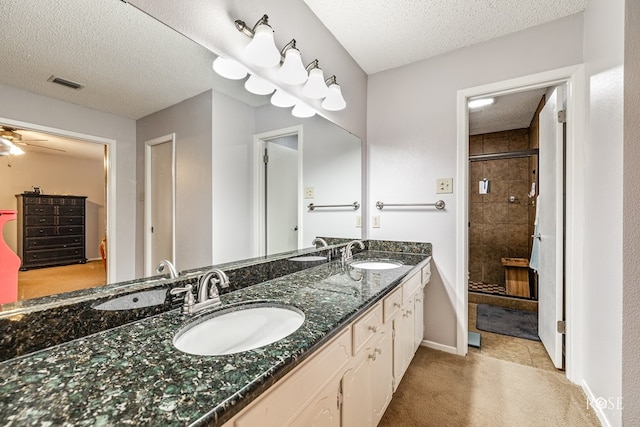 full bathroom with a stall shower, a textured ceiling, visible vents, and a sink