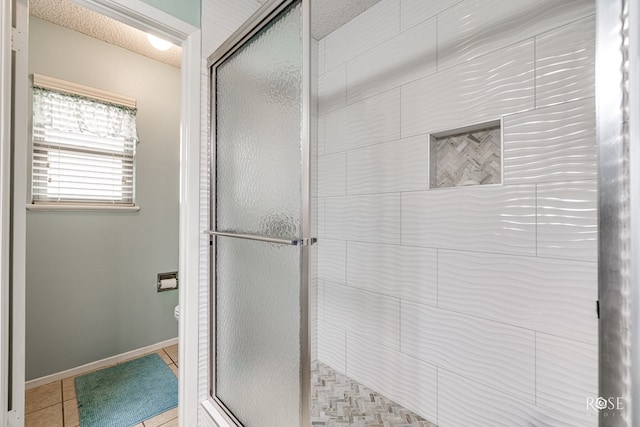 bathroom with toilet, tile patterned flooring, baseboards, and a tile shower