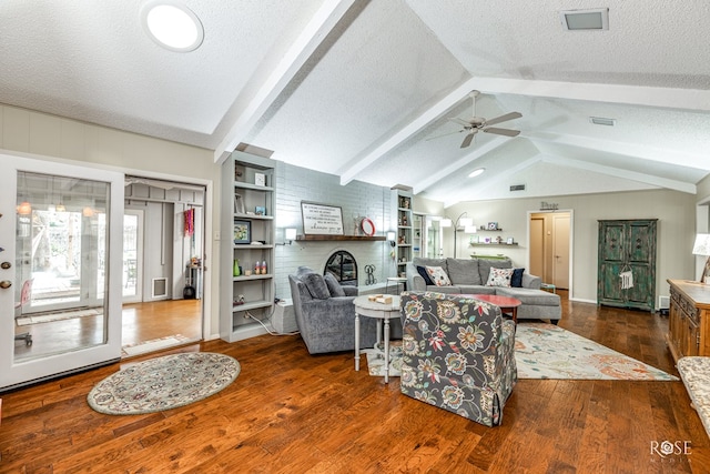 living area with a textured ceiling, lofted ceiling with beams, visible vents, a brick fireplace, and dark wood finished floors