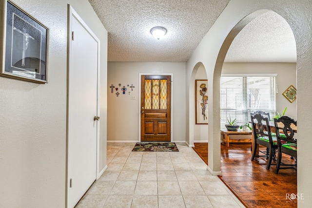 foyer entrance featuring arched walkways, a textured ceiling, baseboards, and light tile patterned floors