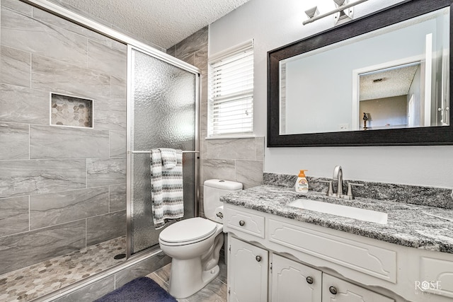 full bathroom with vanity, a shower stall, toilet, and a textured ceiling