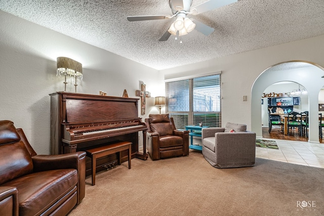 living area featuring arched walkways, carpet, ceiling fan, a textured ceiling, and tile patterned flooring