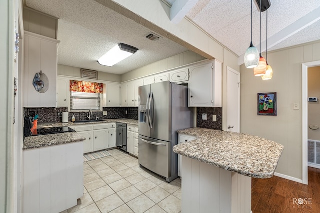 kitchen with a peninsula, a sink, visible vents, tasteful backsplash, and stainless steel fridge