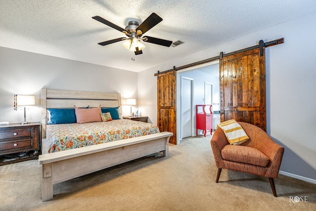 bedroom featuring a textured ceiling, a barn door, visible vents, a ceiling fan, and carpet