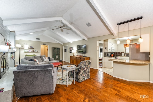 living room featuring vaulted ceiling with beams, a textured ceiling, wood finished floors, and a ceiling fan