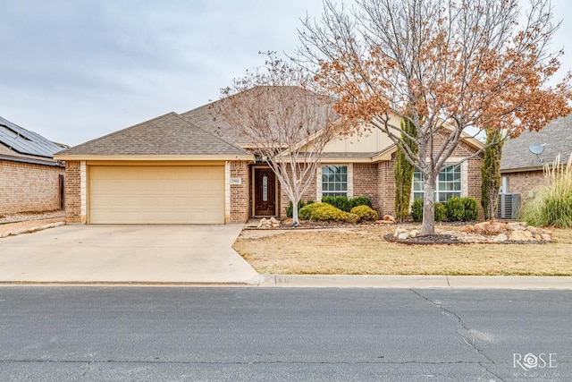 single story home with driveway, a garage, a shingled roof, central air condition unit, and brick siding