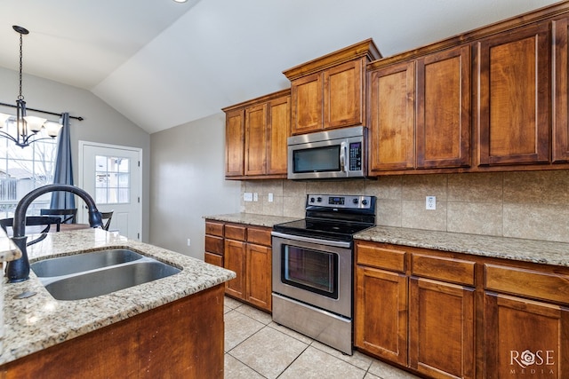 kitchen featuring lofted ceiling, a sink, appliances with stainless steel finishes, light stone countertops, and brown cabinetry