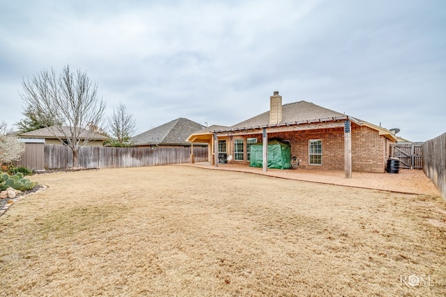 rear view of property with a lawn, a fenced backyard, a chimney, a patio area, and brick siding