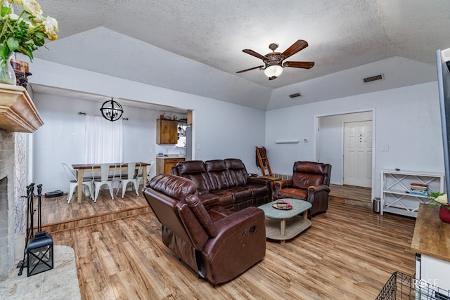 living room with lofted ceiling, a textured ceiling, light hardwood / wood-style floors, and a fireplace