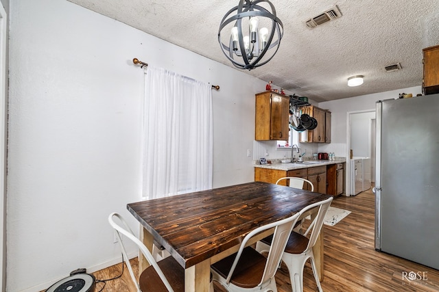 dining room with sink, a chandelier, a textured ceiling, and dark hardwood / wood-style flooring