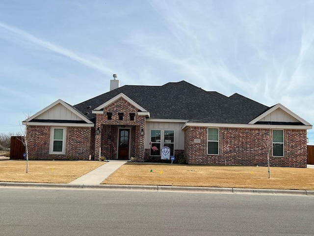 view of front facade with roof with shingles, a chimney, and brick siding