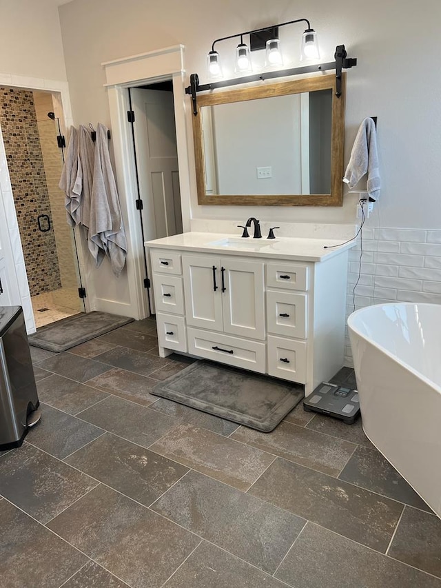 bathroom with stone tile floors, tile walls, vanity, a soaking tub, and a stall shower