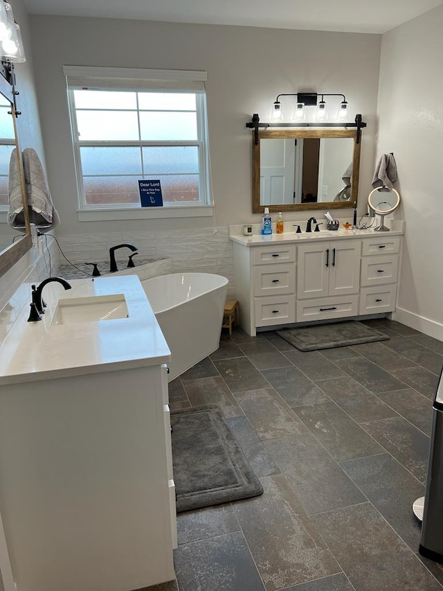 full bathroom featuring stone tile flooring, two vanities, a sink, and a freestanding bath