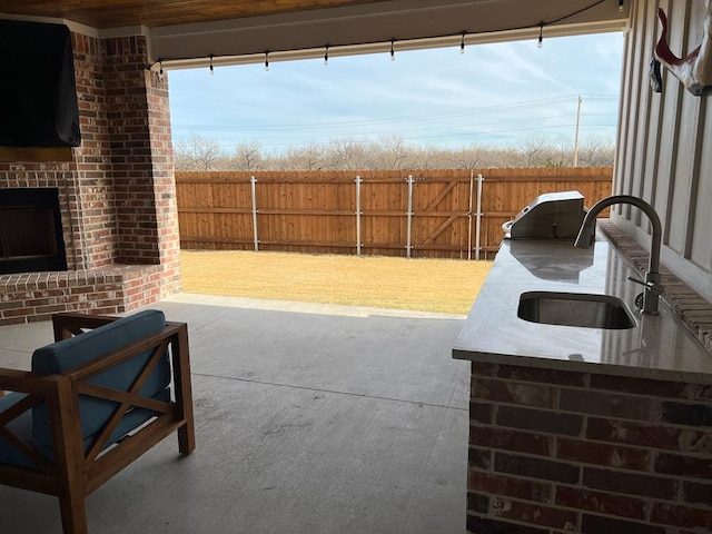 view of patio with an outdoor brick fireplace, a fenced backyard, and a sink