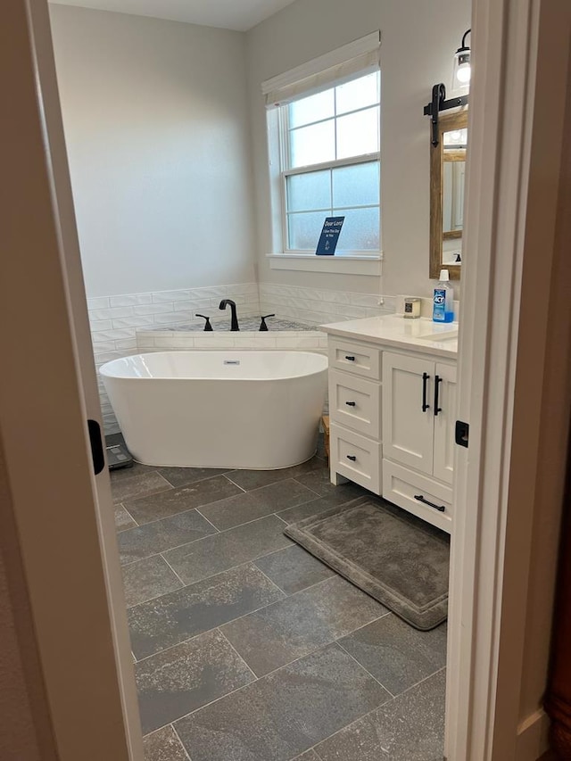 full bathroom featuring a soaking tub, a wainscoted wall, stone tile flooring, vanity, and tile walls