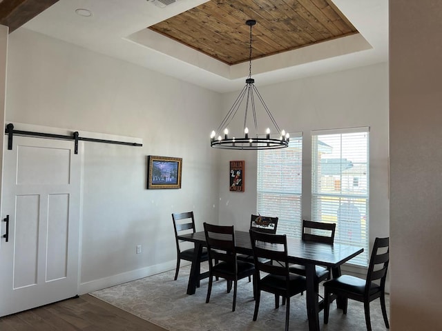 dining space featuring dark wood-type flooring, a barn door, a raised ceiling, and a notable chandelier