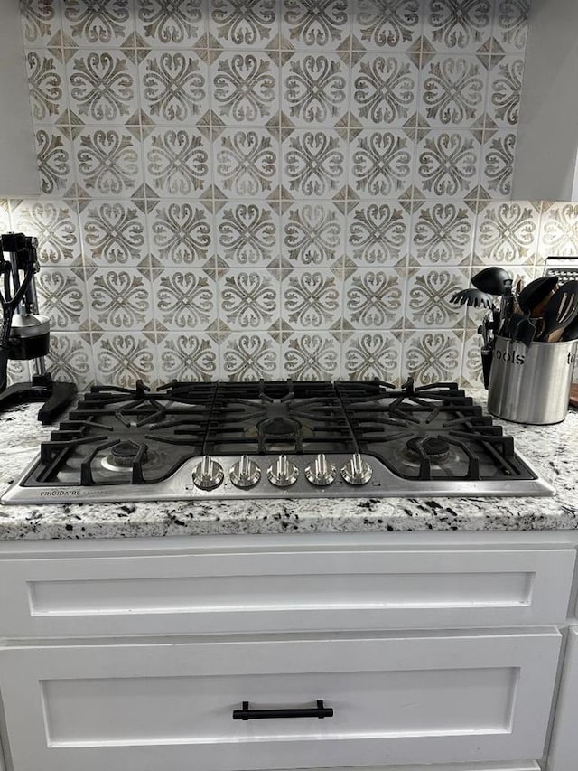 room details with light stone countertops, stainless steel gas cooktop, white cabinets, and backsplash