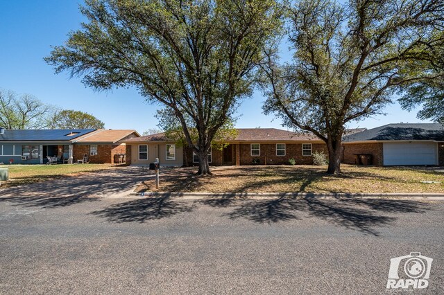 ranch-style house with roof mounted solar panels, brick siding, and dirt driveway