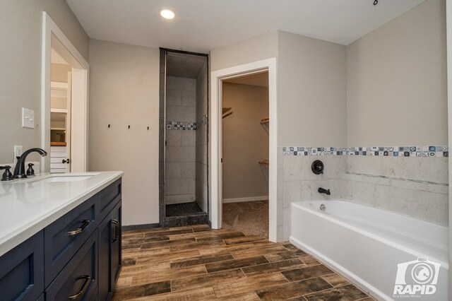 bathroom with a bath, a walk in closet, wood finish floors, vanity, and tiled shower