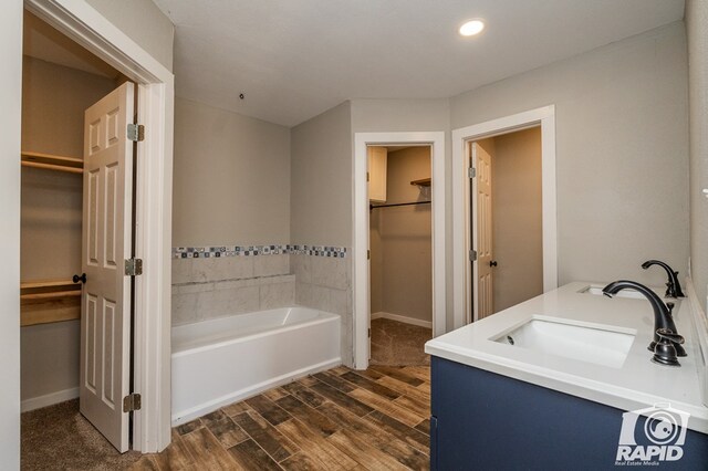 bathroom with a walk in closet, a garden tub, a sink, and wood finished floors