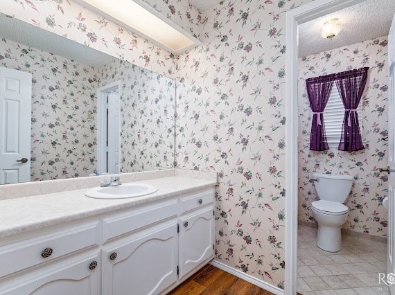 3309 Cedarhill Dr, San Angelo, TX 76904 - bathroom with vanity, baseboards, wallpapered walls, toilet, and wood finished floors
