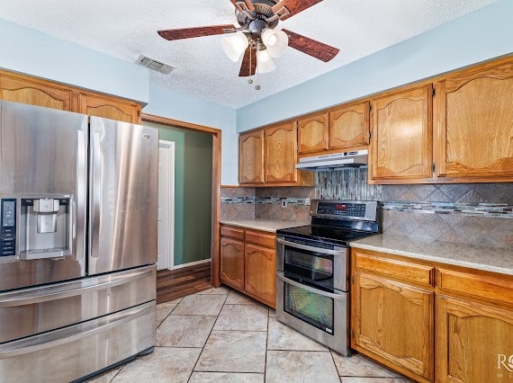 3309 Cedarhill Dr, San Angelo, TX 76904 - kitchen featuring appliances with stainless steel finishes, under cabinet range hood, light countertops, brown cabinetry, and decorative backsplash