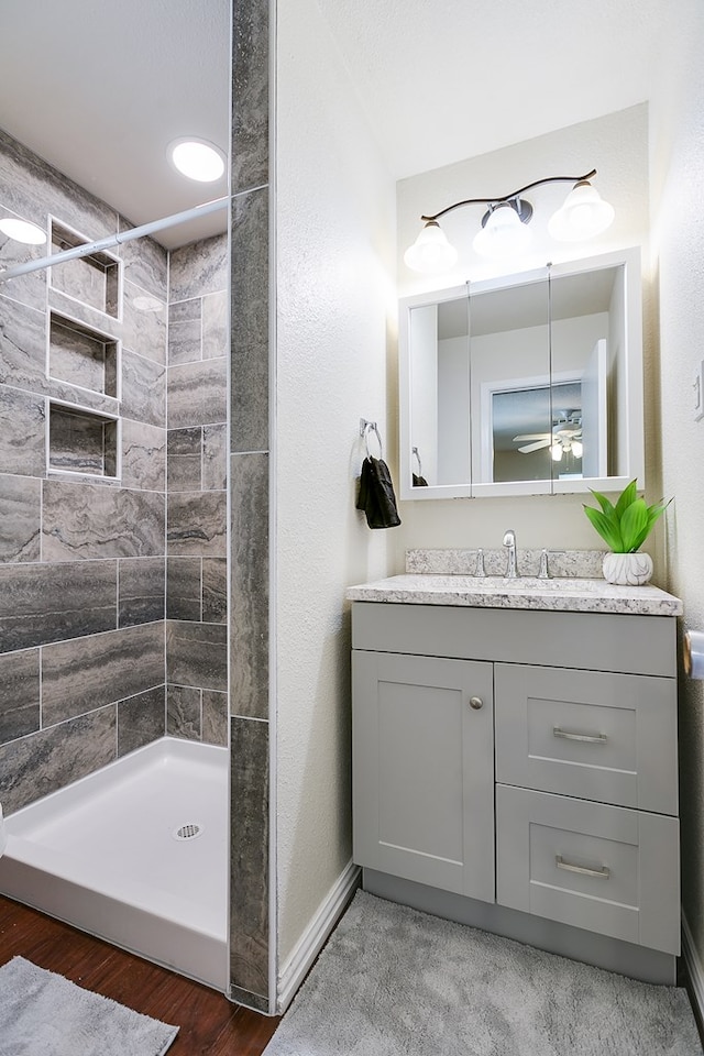 full bath with a tile shower, ceiling fan, vanity, and wood finished floors