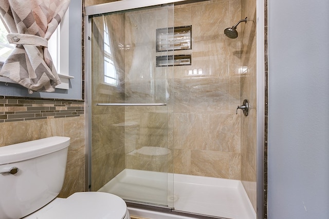 bathroom with toilet, tile walls, and a shower stall