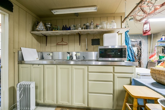 kitchen featuring sink, stainless steel counters, radiator heating unit, cream cabinetry, and wood walls