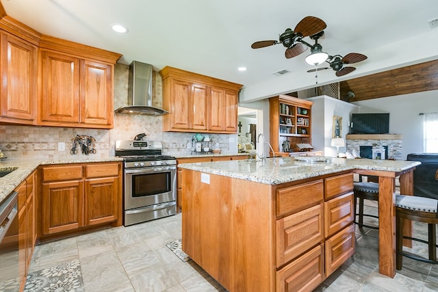 kitchen with beamed ceiling, appliances with stainless steel finishes, light stone counters, and wall chimney exhaust hood