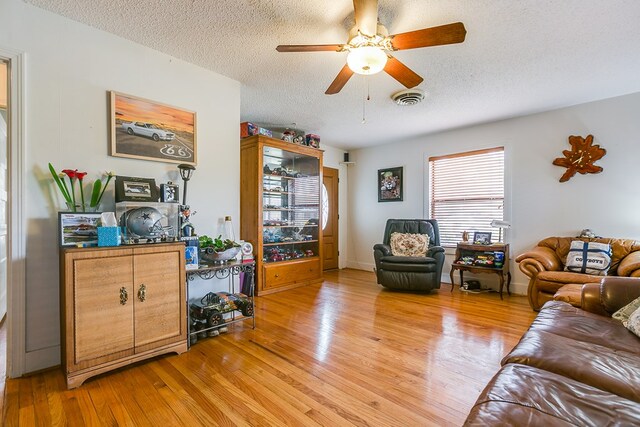 living room featuring ceiling fan, light wood-type flooring, and a textured ceiling