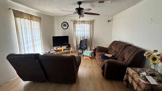 living room featuring ceiling fan, a textured ceiling, and light wood-type flooring