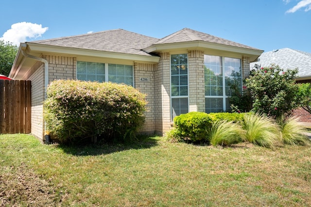 view of property exterior with a yard, brick siding, fence, and roof with shingles