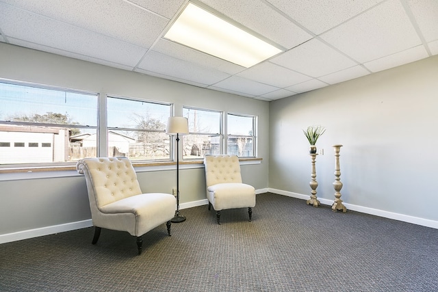 living area featuring dark colored carpet and a paneled ceiling