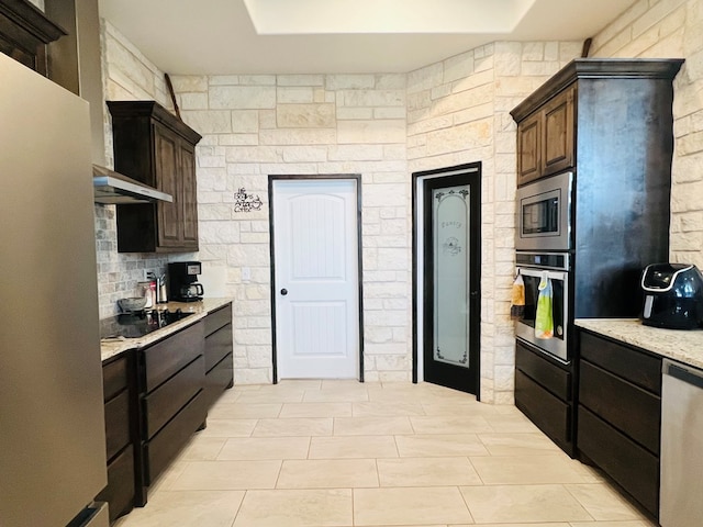 kitchen with stainless steel appliances, light stone countertops, backsplash, and dark brown cabinetry