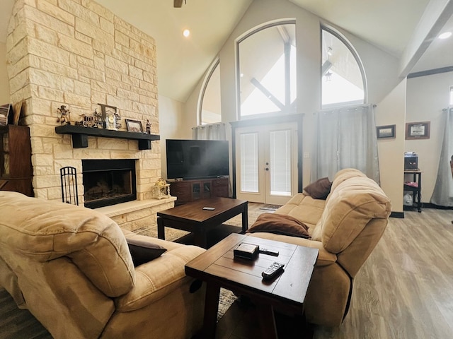 living room featuring a stone fireplace, high vaulted ceiling, french doors, and light wood-type flooring