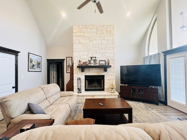 living room with ceiling fan, a stone fireplace, high vaulted ceiling, and light hardwood / wood-style flooring