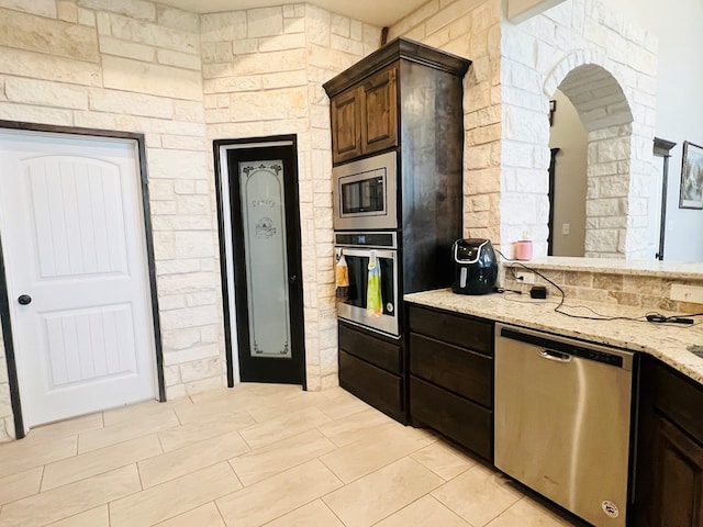 kitchen with appliances with stainless steel finishes, light stone countertops, and dark brown cabinets