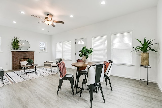 dining room featuring ceiling fan, light wood-type flooring, and a fireplace