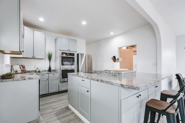 kitchen with sink, a breakfast bar area, light hardwood / wood-style flooring, appliances with stainless steel finishes, and gray cabinets