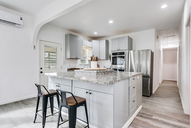 kitchen with a wall mounted AC, a kitchen bar, a center island, stainless steel appliances, and light stone countertops