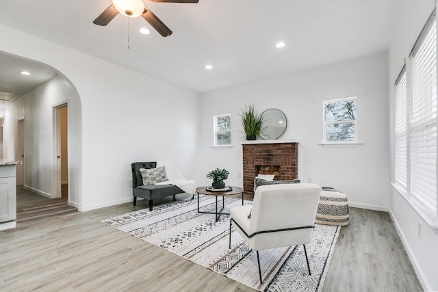 sitting room with a brick fireplace, ceiling fan, and light hardwood / wood-style flooring