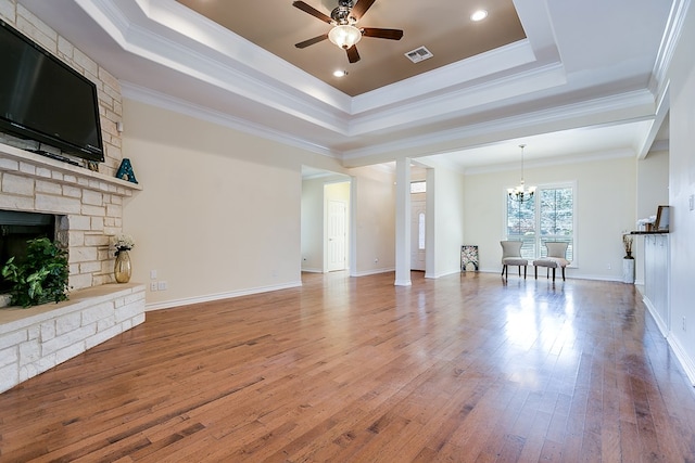 unfurnished living room with ornamental molding, a stone fireplace, and ceiling fan with notable chandelier