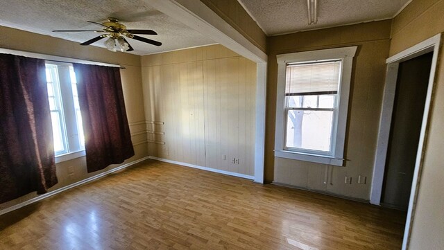 spare room with ceiling fan, hardwood / wood-style floors, a textured ceiling, and wood walls