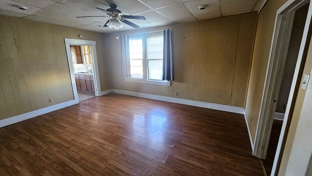 spare room with sink, a paneled ceiling, ceiling fan, dark hardwood / wood-style floors, and wood walls