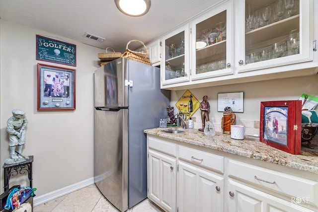 kitchen featuring light tile patterned flooring, visible vents, freestanding refrigerator, light stone countertops, and glass insert cabinets