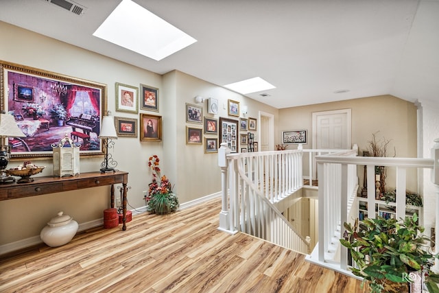 hall featuring a skylight, wood finished floors, visible vents, an upstairs landing, and baseboards