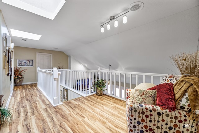 sitting room with vaulted ceiling with skylight, visible vents, wood finished floors, and an upstairs landing