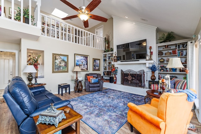 living area with a ceiling fan, a brick fireplace, wood finished floors, high vaulted ceiling, and baseboards