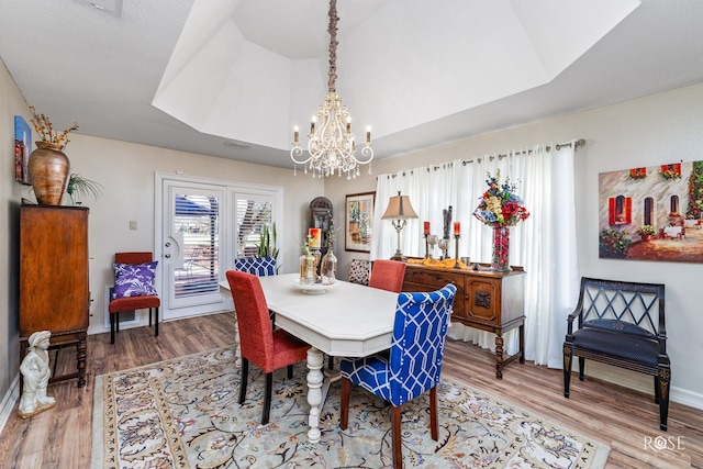 dining area with a chandelier, light wood-style flooring, baseboards, vaulted ceiling, and a tray ceiling